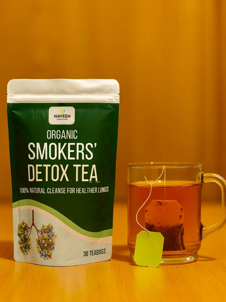 Naveen Mullein Smokers’ Detox Tea pouch beside a clear glass cup of brewed tea on a wooden surface with a warm, golden background.