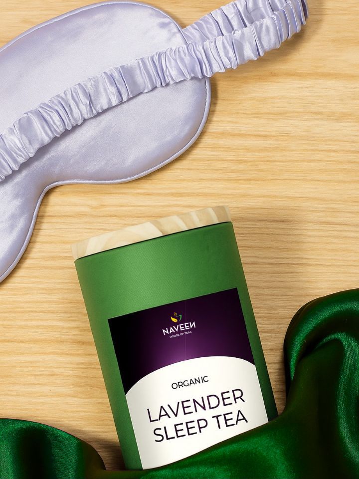 A tin of Naveen Lavender Sleep Tea placed beside a silk sleep mask on a wooden surface, representing rest, serenity, and nighttime relaxation.