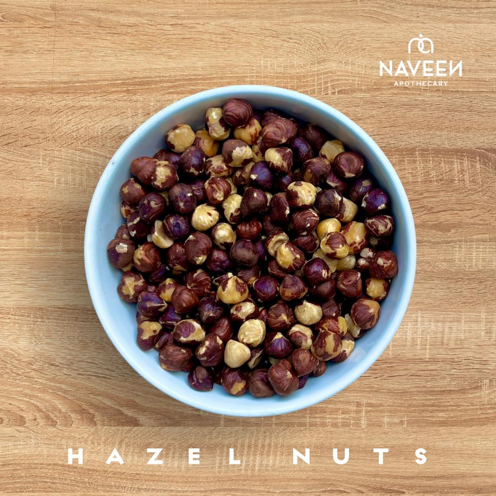 A bowl of whole hazelnuts on a wooden surface with the Naveen Apothecary logo.