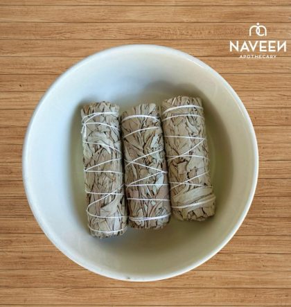 Three bundled white sage sticks tied with string in a bowl on a wooden surface with the Naveen Apothecary logo.
