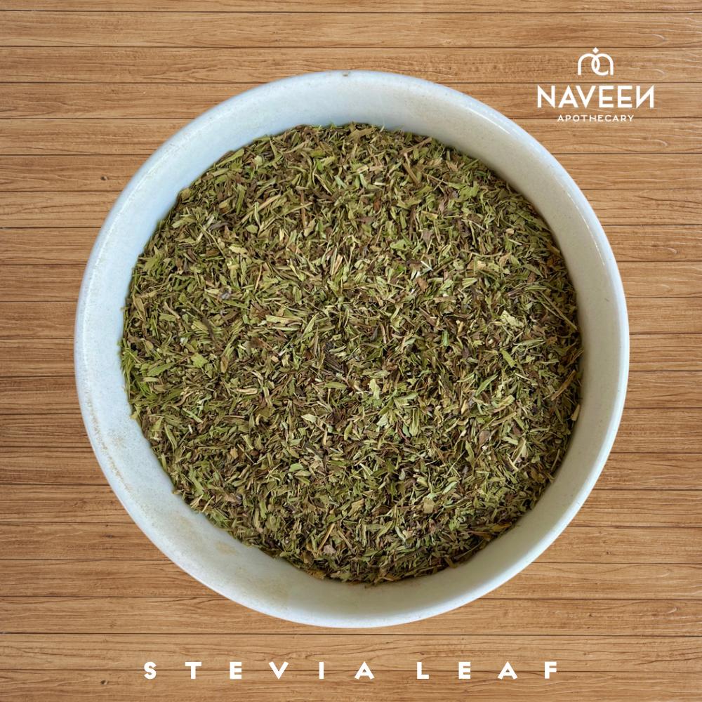 A bowl of dried stevia leaf pieces on a wooden surface with the Naveen Apothecary logo.