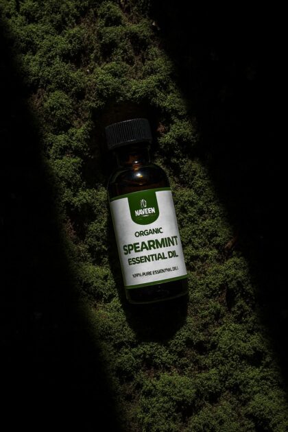 Bottle of organic spearmint essential oil by Naveen Herbs Co placed on natural moss surface highlighting pure herbal essential oil for aromatherapy and wellness